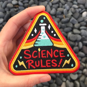 May include: A red, yellow, and black triangular patch with an embroidered image of a beaker and the text "Science Rules!"