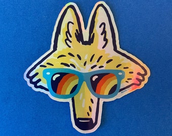 May include: A holographic sticker featuring a stylized coyote head wearing blue sunglasses with a rainbow design. The coyote is yellow and white with black outlines, set against a blue background. The sticker has a glossy finish.