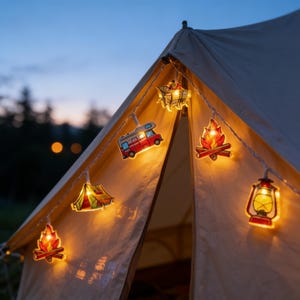 Puede incluir: Una cadena de luces decorativa con temática de camping, que incluye una autocaravana roja, una fogata, una tienda de campaña y una linterna. Las luces están colgadas sobre una tienda de campaña beige, iluminadas contra un cielo crepuscular. Funciona con pilas.