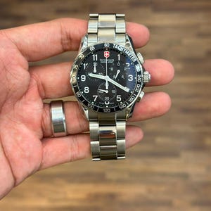 May include: A stainless steel Victorinox Swiss Army chronograph watch with a black dial, white Arabic numerals, three sub-dials, and a tachymeter scale on the bezel. The watch features a metallic link bracelet and luminous hands for timekeeping.