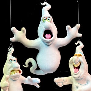 Könnte beinhalten: Drei weiße Cartoon-Geister mit ausdrucksstarken Gesichtern und offenem Mund hängen vor einem schwarzen Hintergrund. Ein Geist hat einen weit geöffneten Mund mit rosa Zunge, ein anderer lacht und der dritte runzelt die Stirn.