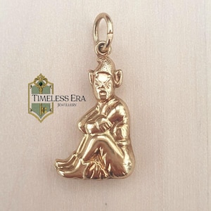 Puede incluir: Un dije dorado con forma de gnomo sentado con los brazos cruzados. El dije tiene un lazo en la parte superior para sujetarlo a un collar o pulsera. El dije es de Timeless Era Jewellery.