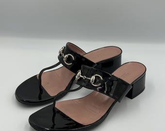 Sandalias tipo mule Gucci de charol negro con detalle de estribo y tira en T, tacón bajo.
