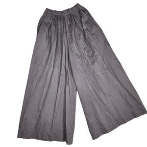 May include: A pair of wide-leg trousers in a solid dark gray color. These pants feature an elasticized waistband with gathered fabric detailing, creating a loose, flowing silhouette that extends down to a straight hemline at the bottom of the legs.