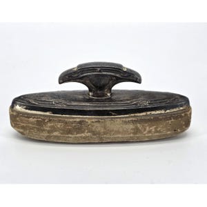 May include: An antique silver-toned ink blotter with a decorative handle. The blotter has an oval shape with a worn, tan blotting surface. The handle features an ornate design.