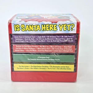 May include: A red box set of Christmas cassette tapes. The box reads "IS SANTA HERE YET?" with a list of Christmas songs on the cassette labels, including "Jingle Bells" and "Silent Night".