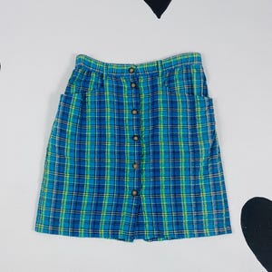 May include: A blue and green plaid skirt with a button front fastening. The skirt has two pockets on the sides.