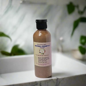 May include: A brown bottle of herbal shampoo with a black cap. The label reads "HERBAL SHAMPOO ORGANIC" and lists benefits like repairing damaged hair and promoting growth. The bottle is on a white surface.