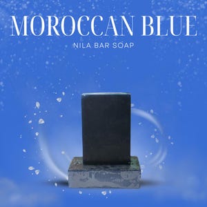 Può includere: Una saponetta Nila blu scuro è appoggiata su una base quadrata grigio scuro su sfondo blu. Le parole "MOROCCAN BLUE" e "NILA BAR SOAP" sono visualizzate in testo bianco nella parte superiore dell'immagine.