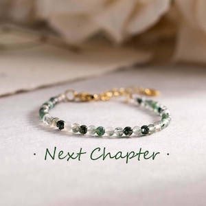 Op de afbeelding: Een delicate armband met kleine, ronde groene en heldere kralen, geregen op een goudkleurige ketting. De armband wordt gepresenteerd op een wit oppervlak met de tekst "Next Chapter" in een zachtgroene letter.