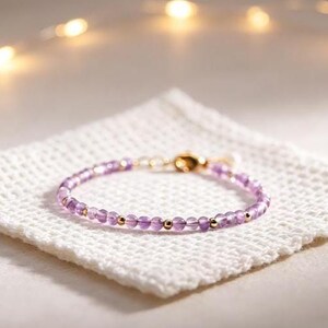 Puede incluir: Una pulsera delicada con pequeñas cuentas redondas de amatista púrpura translúcida intercaladas con diminutas esferas de metal en tono dorado pulido. La pulsera cuenta con un cierre de mosquetón de metal dorado y una cadena extensora.