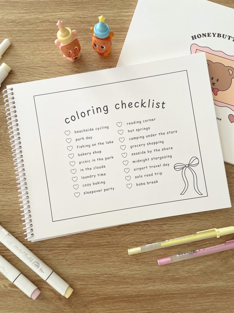 May include: A spiral-bound coloring checklist notebook with the words "coloring checklist" at the top. The checklist includes activities like "beachside cycling" and "boba break." Two small toy figures and several colored pens are also visible.
