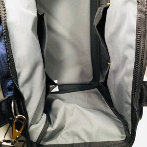 May include: Black and blue tool bag with multiple interior pockets and a gray lining. The bag has a black zipper, a shoulder strap, and metal hardware. The bag is designed for carrying tools and equipment.