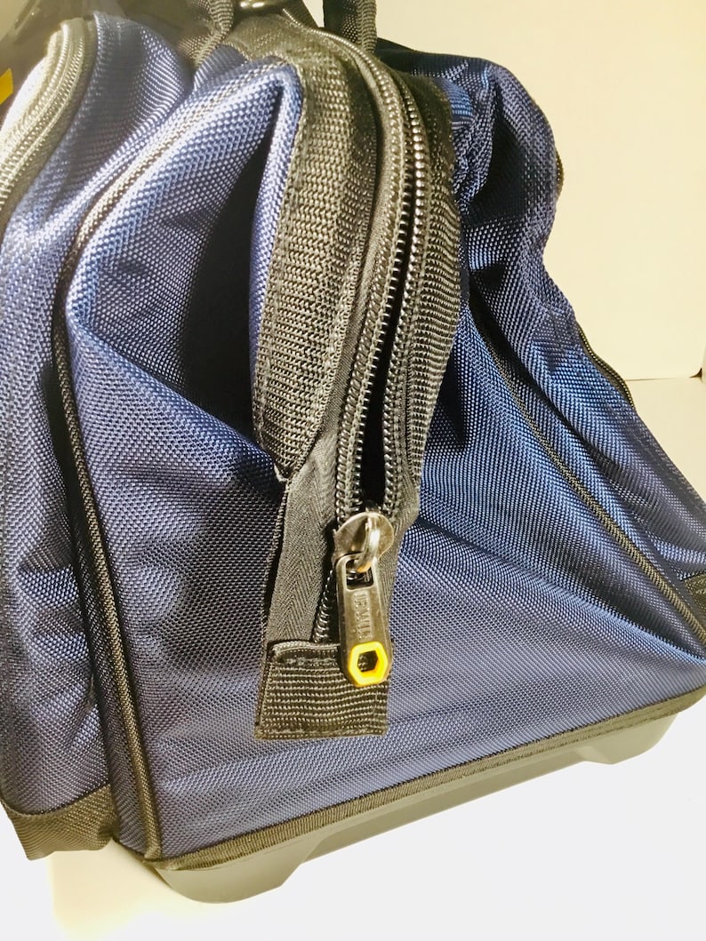 May include: Close-up of a navy blue rolling tool bag with black trim and zippers. The bag has a textured fabric and a yellow accent on the zipper pull. The bag appears to be new and unused.