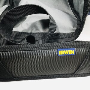 May include: Close-up of a black tool bag with a textured front panel and a black handle. The bag has a blue and yellow "IRWIN" logo. The interior of the bag is visible, with a gray lining.