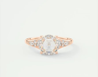 May include: Rose gold ring featuring a large, clear, faceted gemstone as the centerpiece. Smaller, clear gemstones are set on either side of the main stone. The ring has a delicate, elegant design, perfect for engagement or special occasions.