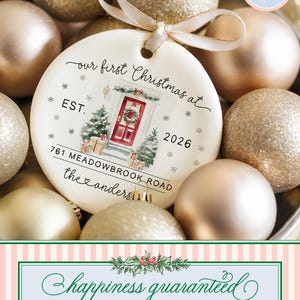May include: A round white ceramic Christmas ornament featuring a watercolor illustration of a red front door with a wreath, two small Christmas trees, and gift boxes. Text reads: our first Christmas at EST. 2026 761 MEADOWBROOK ROAD the anders.