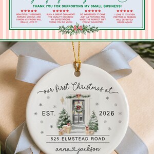 May include: A round white ceramic ornament featuring a watercolor illustration of a front door with a wreath, two Christmas trees, and wrapped gifts. The text reads: our first Christmas at, EST. 2026, 525 ELMSTEAD ROAD, and anna and jackson.