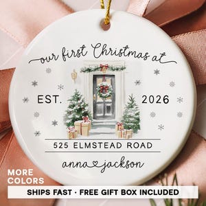 May include: A round white ceramic ornament featuring a watercolor illustration of a front door with a wreath, two Christmas trees, and wrapped gifts. The text reads: our first Christmas at EST. 2026 525 ELMSTEAD ROAD anna & jackson.