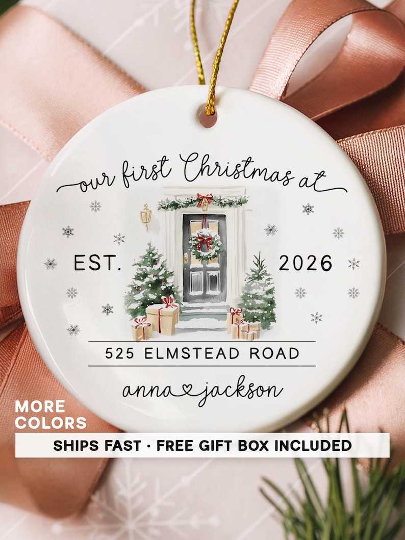 May include: A round white ceramic ornament featuring a watercolor illustration of a front door with a wreath, two Christmas trees, and wrapped gifts. The text reads: our first Christmas at EST. 2026 525 ELMSTEAD ROAD anna & jackson.