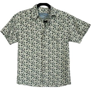 May include: Short-sleeved button-down shirt with a cream-colored background and a repeating pattern of dark green shapes. The shirt has a chest pocket and a classic collar. The shirt is hanging on a black hanger.