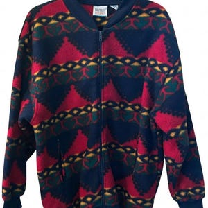 May include: A zip-up fleece jacket with a vibrant geometric pattern in red, navy blue, green, and yellow. The jacket features a navy blue collar, cuffs, and hem, and a full-length zipper. The jacket has a label that reads "Margaret Interpret".