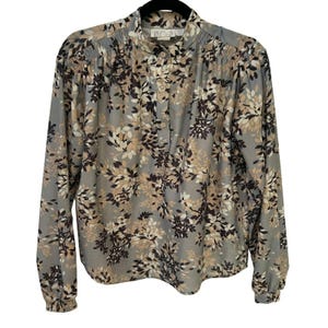 Op de afbeelding: Een blouse met lange mouwen met een grijze achtergrond en een bloemenpatroon in bruin-, beige- en wittinten. De blouse heeft een opstaande kraag, een knoopsluiting en geplooide details op de schouders.