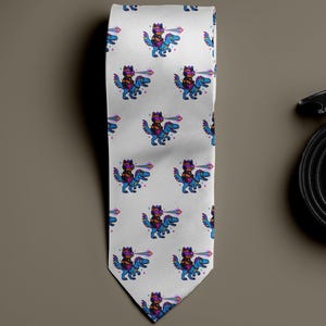May include: White necktie with a repeating pattern of a cartoon character riding a dinosaur, in blue, purple, and pink. A rolled-up black leather belt with a silver buckle is next to the tie.