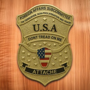 May include: A gold-colored metal badge with the text "FOREIGN AFFAIRS SUBCOMMITTEE" and "U.S.A." The badge features an American flag design and the words "DONT TREAD ON ME" and "ATTACHE".