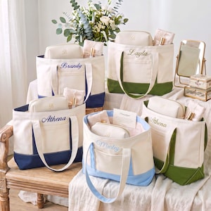 May include: A collection of five canvas tote bags with matching zippered pouches. Each bag features a cream-colored upper section, a solid-colored base in navy, olive green, or light blue, and personalized embroidery with names like Brandy, Layla, Athena, and Marley.