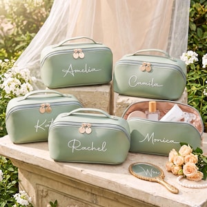 May include: Five sage green cosmetic bags with top handles and gold circular zipper pulls. Four bags are closed and personalised with white script names: Amelia, Camila, Kate, and Rachel. One open bag labelled Monica contains toiletries and a hand mirror.