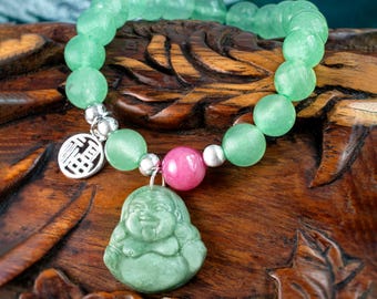 Op de afbeelding: Een groene jade armband met een roze jade kraal en een zilveren bedel met het Chinese karakter voor "geluk". De armband is versierd met een groene jade hanger van een lachende Boeddha.