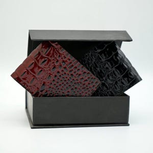 May include: A black gift box containing two wallets, one red and one black. Both wallets have a crocodile skin effect. The red wallet is on the left, the black on the right. The box is open, displaying the wallets within.