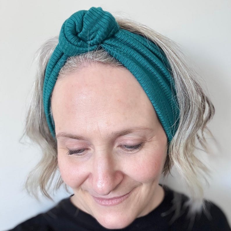 Peut inclure: Un bandeau en tricot c&ocirc;tel&eacute; vert teal avec un n&oelig;ud sur le dessus. Le bandeau est fait d'une mati&egrave;re douce et extensible et se porte sur la t&ecirc;te. La femme sur l'image porte un haut noir.
