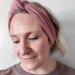 Peut inclure: Un bandeau en tricot c&ocirc;tel&eacute; rose poudr&eacute;. Le bandeau est nou&eacute; sur le dessus et s'enroule autour de la t&ecirc;te. Le tissu a un aspect textur&eacute;. Le bandeau est un accessoire pour cheveux.