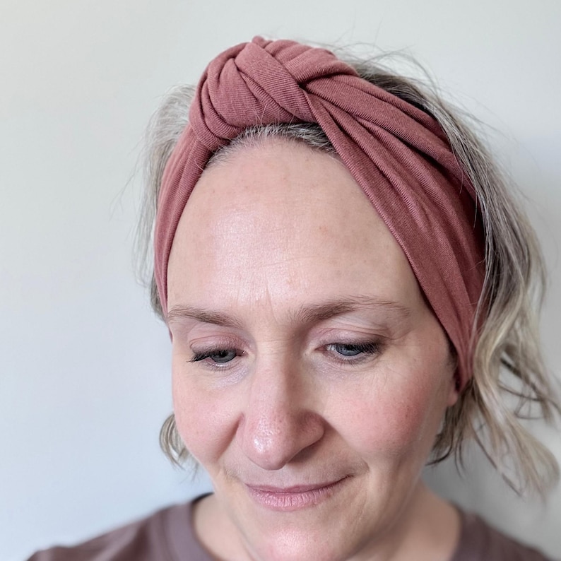 Peut inclure: Un bandeau nou&eacute; de couleur rose poussi&eacute;reux. Le large bandeau est fait d'un tissu doux et extensible et se porte sur le front. Le bandeau est de couleur unie et pr&eacute;sente un d&eacute;tail de n&oelig;ud torsad&eacute; sur le dessus.