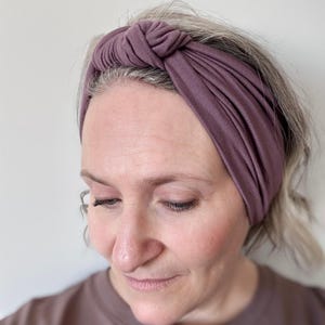 Peut inclure: Un bandeau nou&eacute; de couleur mauve. Le bandeau est fait d'un tissu doux et extensible et est con&ccedil;u pour &ecirc;tre port&eacute; autour de la t&ecirc;te. Le d&eacute;tail du n&oelig;ud ajoute une touche &eacute;l&eacute;gante. Le bandeau est de couleur unie et semble neuf.