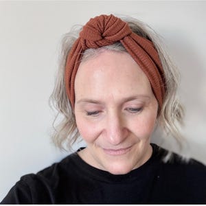 Peut inclure: Un bandeau en tricot c&ocirc;tel&eacute; de couleur rouille avec un dessus nou&eacute;. Le bandeau est fait d'un mat&eacute;riau doux et extensible et est con&ccedil;u pour &ecirc;tre port&eacute; autour de la t&ecirc;te. Le bandeau est un accessoire &eacute;l&eacute;gant.