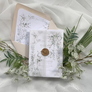 May include: A white wedding invitation with a green floral design and a wax seal. The invitation is on a white background with a white sheer fabric overlay.