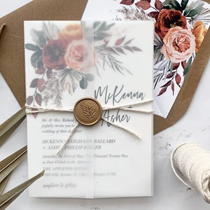 Puede incluir: Una invitación de boda con un diseño floral de acuarela en tonos rojos, naranjas y marrones. La invitación está atada con un cordel y tiene un sello de cera. El texto de la invitación dice: "Mr. & Mrs. Richard les invitan con alegría a la boda de su hija McKenna Asher".