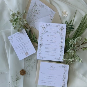 May include: A wedding invitation suite with a floral design. The invitation features a white background with a floral border and the text "Together with their families Penelope Michelle Smith and Matthew Patrick Forester Saturday, the Fifth of June Two Thousand Twenty-Five at Four O'Clock in the Afternoon Farmhouse Winery Cellars 42 Church Street St. Charles, Missouri reception to follow". The RSVP card features a white background with a floral border and the text "Kindly respond by May 1, 2021. Accepts with Pleasure Declines with Regret Please meal selection for each guest: Prime Rib, Chicken, Salmon".
