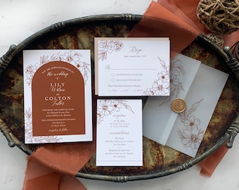 May include: Wedding invitation suite with a floral design in a rust color. The invitation features a floral arch with the text "You are joyfully invited to the wedding of Lily Wilson and Colton Fuller." The RSVP card has a floral design and the text "RSVP Kindly respond by May 1, 2017."