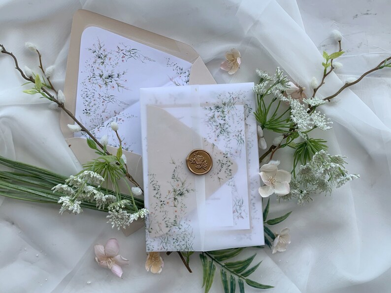 May include: A set of two wedding invitations with a delicate floral design. The invitations are on a white background with a light brown envelope. The envelope has a wax seal with a floral design.