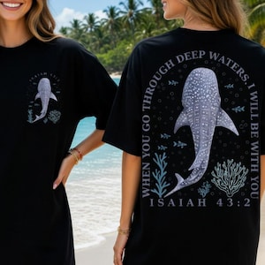 May include: Black t-shirt featuring a whale shark design. The front of the shirt has a small whale shark graphic with the text "Isaiah 43:2". The back of the shirt has a larger whale shark graphic with the text "When you go through deep waters, I will be with you. Isaiah 43:2".