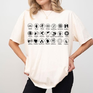 May include: Cream-colored t-shirt with a black graphic featuring various symbols and text. The text includes words like "Empath," "Shade," and "Phaser." The design is arranged in circular patterns across the front of the shirt.