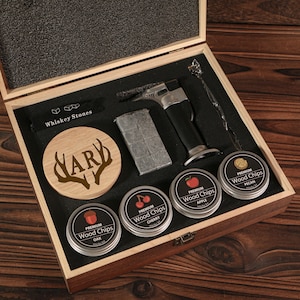 Puede incluir: Un juego de regalo de madera para entusiastas del whisky. El juego incluye piedras de whisky, un soplete, una cuchara para remover, un posavasos de madera con "HARY" y astas, y latas de virutas de madera con etiquetas.