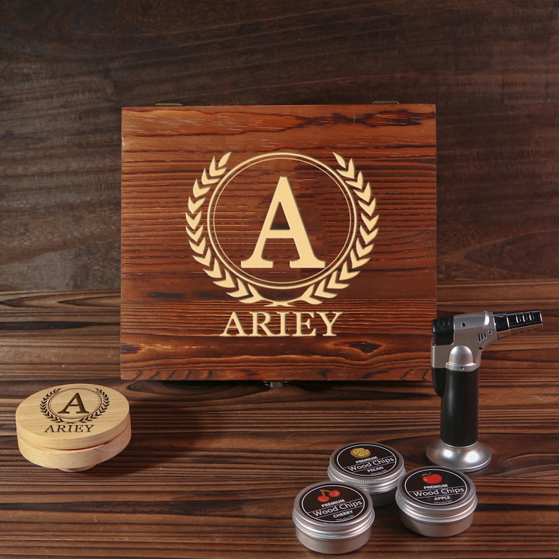 May include: A wooden box with the letter "A" and the name "ARIEY" engraved on the lid, along with a small wooden container with the same design. Also included are three small tins of wood chips and a black and silver torch.