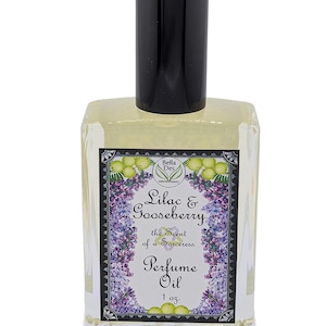 Op de afbeelding: Een heldere glazen parfumolie fles met een zwarte dop. Het etiket luidt "Lilac & Gooseberry, the Scent of a Sorceress, Perfume Oil, 1 oz." met bloemen- en fruitillustraties. De fles bevat een lichtgele vloeistof.