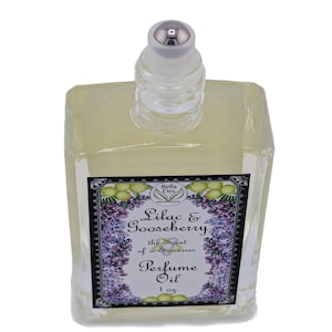 Op de afbeelding: Een heldere, rechthoekige parfumolie fles met een zilveren dop. Het etiket toont de tekst "Lilac & Gooseberry" en "Perfume Oil" met bloemen- en bladerillustraties. De fles bevat 29.57 ml parfumolie.