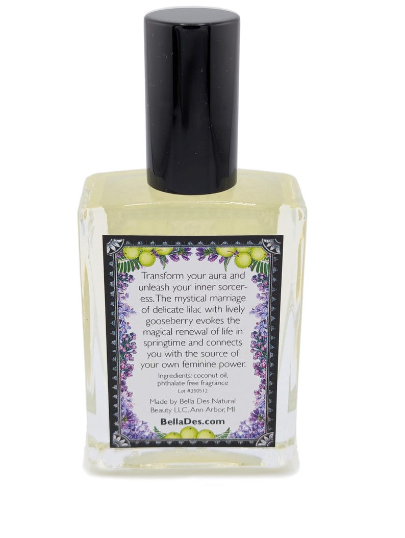 Op de afbeelding: Een heldere glazen parfumfles met een zwarte dop. Het etiket bevat tekst en illustraties van sering en kruisbessen. De tekst op het etiket luidt "Transformeer je aura..." en "BellaDes.com".